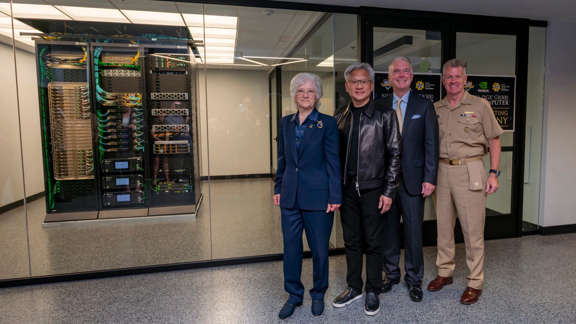 Four individuals pose in front of a large server rack with visible colorful cables and hardware; a sign behind them reads 'NVIDIA DGX GB300 COMPUTER' alongside NPS and NVIDIA logos.