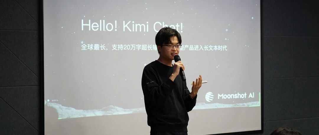 一名戴眼镜的男子手持麦克风在演讲，身后投影屏幕显示'Hello! Kimi Chat!'及'全球最长，支持20万字超长输入'，右下角有'Moonshot AI'标志。